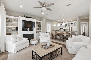 Una sala moderna con mobiliario blanco, una chimenea y un comedor con una cocina al fondo.