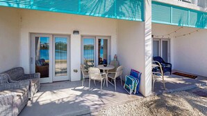 En overdækket terrasse med et bord og stole, en fletsofa og en blå stol.