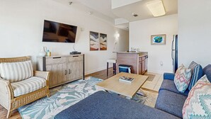 En stue med sofa, sofabord og spiseområde, hvor et køkken ses i baggrunden.