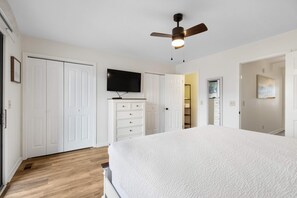 A bedroom with a large bed, white wardrobe, a ceiling fan, and a TV on the wall. - Sweet Townhome with a Patio & Balcony - Just a Half Block from the Beach (Panama City Beach)