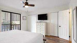 Un dormitorio con cama, ventilador de techo, cómoda, televisor y puerta corrediza.