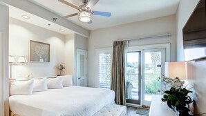 A bedroom with a large bed, a ceiling fan, a window with curtains, and a bedside table with a lamp and flowers. - Lakefront, ground-floor condo with pools & hot tubs - walk to the beach (Panama City Beach)