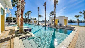 A swimming pool with palm trees, a white building, and a view of the water. - Lakefront, ground-floor condo with pools & hot tubs - walk to the beach (Panama City Beach)