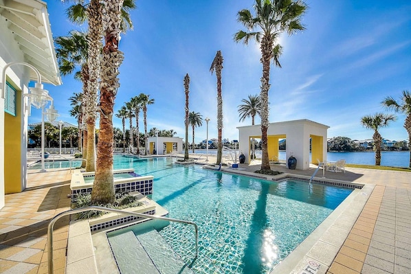 A swimming pool with palm trees, a white building, and a view of the water.