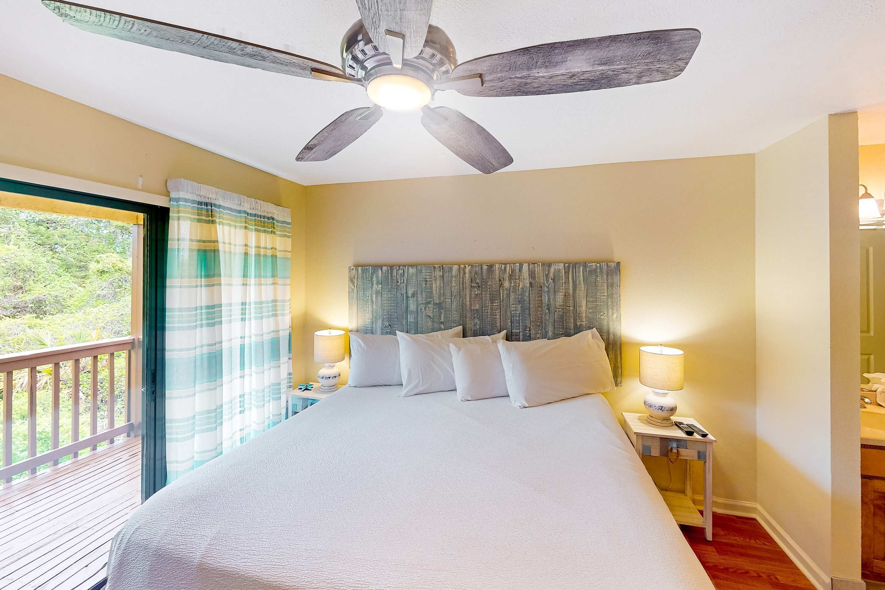 Un dormitorio con una cama grande, dos lámparas de noche, un ventilador de techo y vistas al exterior.