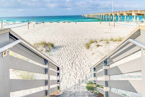 A beach with a pier extending into the ocean, a staircase leading down to the beach, and a sandy path. - Sunny condo near the sand with pool, hot tub, tennis, smart TV, W&D, & AC (Panama City Beach)
