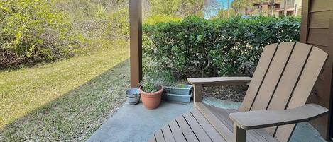 A wooden deck with a chair and a small table, surrounded by a garden and a hedge.