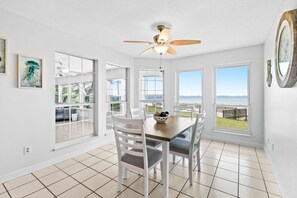 A dining area with a table and chairs, large windows with a view, and a ceiling fan. - Sound-front beauty minutes from beach & pier with private washer&dryer & patio (Navarre)