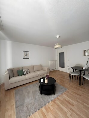A modern living room with a sofa, a coffee table, a dining table with chairs, a radiator, and a door. - Beautiful Apartment Opposite the Train Station (Kassel)