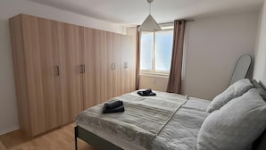 A bedroom with a bed, a wardrobe, a radiator, and a window with curtains. - Beautiful Apartment Opposite the Train Station (Kassel)