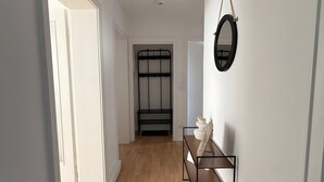 A hallway with wooden flooring, a black metal bench, a round mirror, and a door leading to another room. - Beautiful Apartment Opposite the Train Station (Kassel)