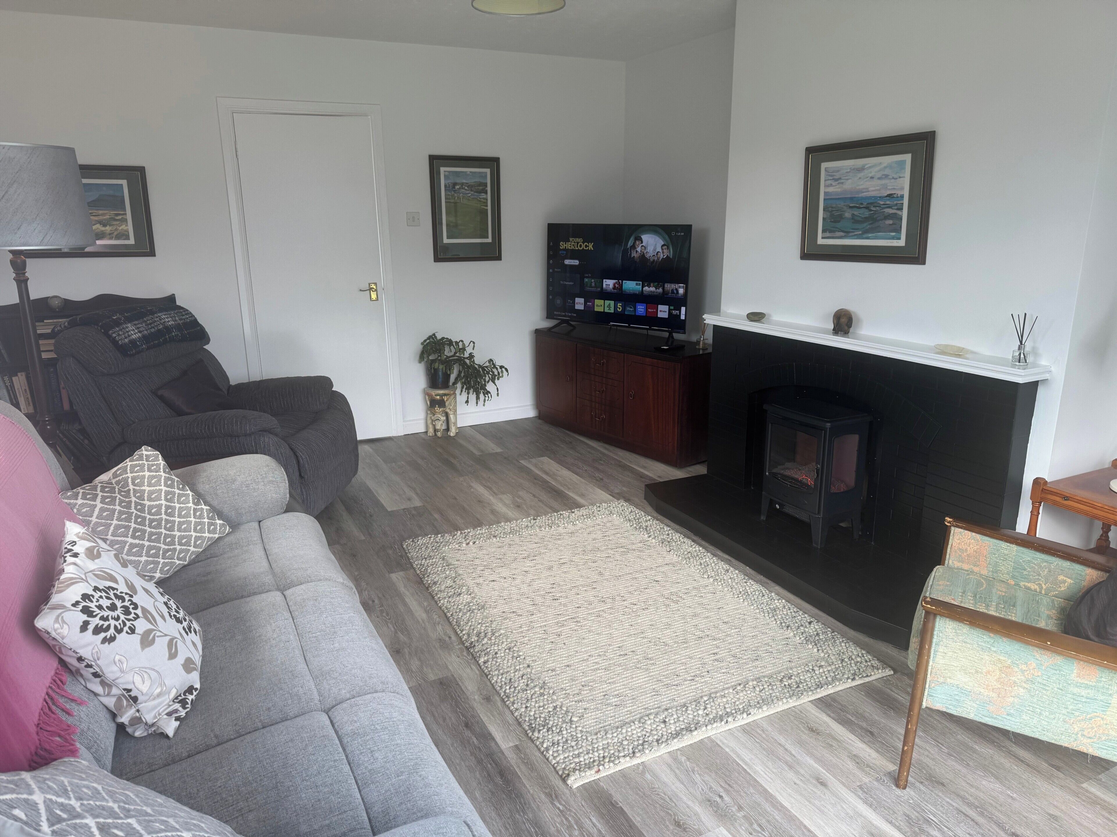 A living room with a grey sofa, a fireplace, a television, and framed pictures on the wall.