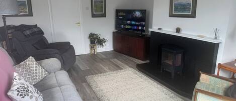A living room with a grey sofa, a fireplace, a television, and framed pictures on the wall.