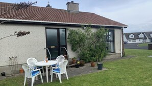 Een huis met een pannendak, een voordeur en een klein terras met een tafel en stoelen.