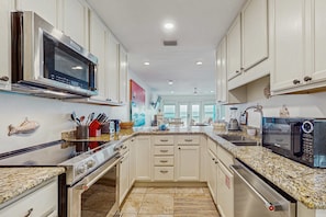 A modern kitchen with white cabinetry, stainless steel appliances, granite countertops, and a view to the outside. - Beautiful beachfront townhome, large deck and beach access (Panama City Beach)