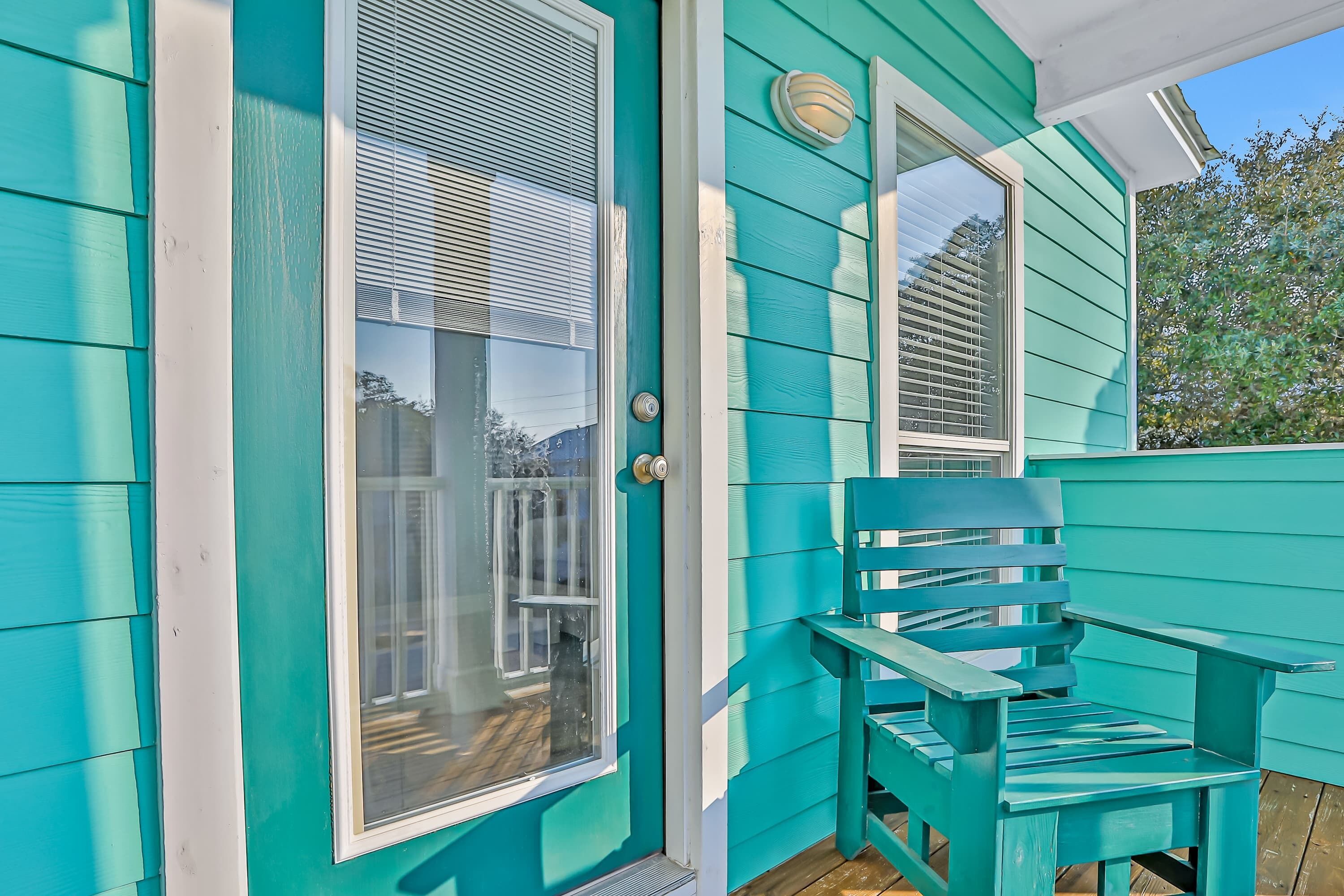 Fachada color turquesa con puerta corrediza de vidrio y terraza de madera.