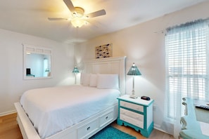 A bedroom with a bed, a nightstand, a lamp, a ceiling fan, a window with curtains, and a wall-mounted mirror. - Bright condo with pool & hot tub access, WiFi, washer/dryer & central AC (Panama City Beach)