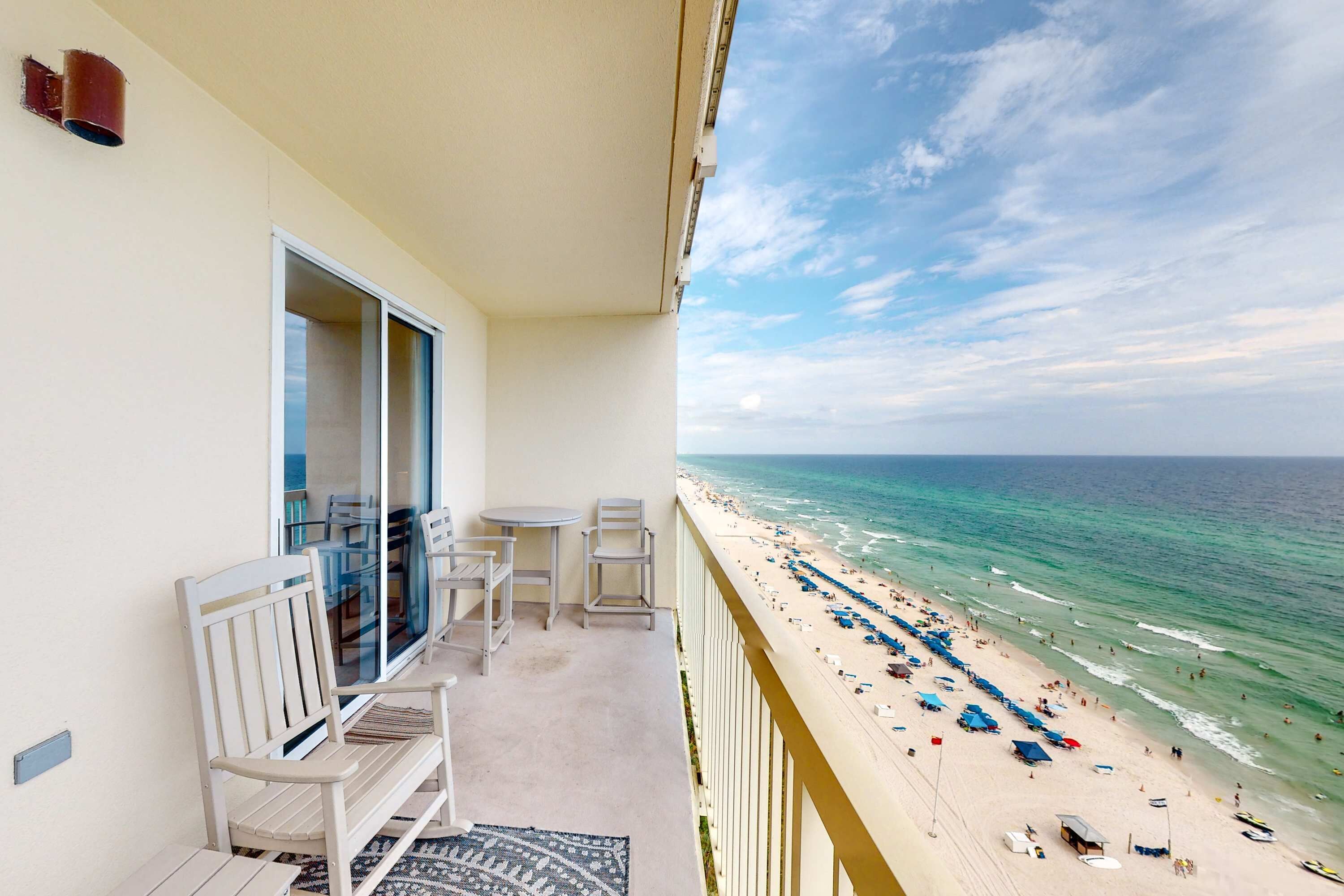 Een balkon met uitzicht op een strand, een klein zitgedeelte met stoelen en een tafel.