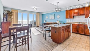 A spacious kitchen with wooden cabinets, a central island, and a dining area with chairs. - Beachfront condo with access to 5 pools, hot tub, fast WiFi, patio, washer/dryer (Panama City Beach)