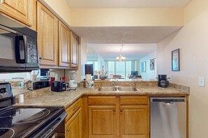 A kitchen with wooden cabinets, a microwave, a stove, a dishwasher, and a granite countertop. - Bright waterfront condo in a gated resort with pools, tennis courts, & gym (Panama City Beach)