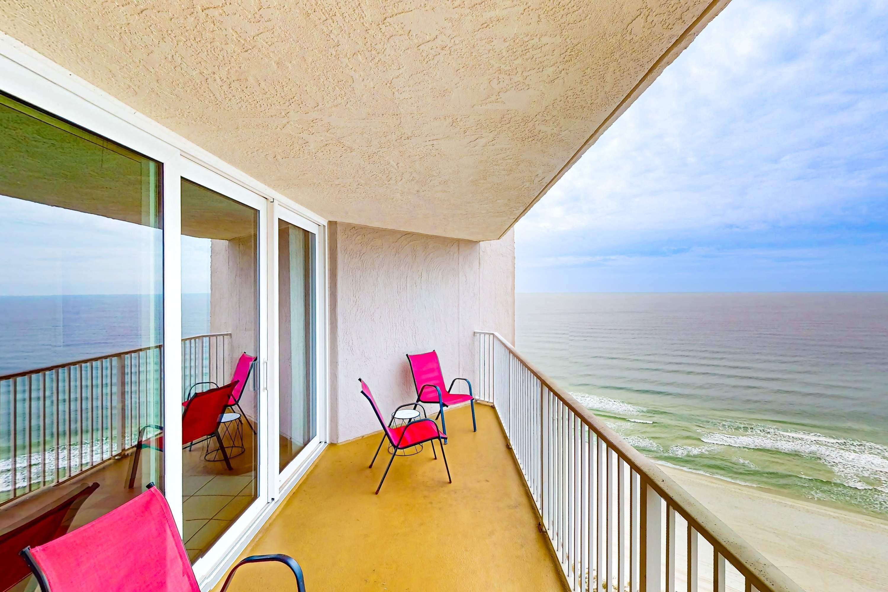 A balcony with a view of the ocean, featuring two red chairs and a glass door.