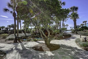 A paved pathway surrounded by various trees and shrubs, leading to a building with a covered entrance. - Terrific condo in beachfront location with pool, central AC & balcony (Panama City Beach)