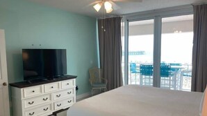 A hotel room with a bed, a TV, a dresser, a chair, and a balcony with outdoor furniture. - Waterfront Condo with Balcony, Washer/Dryer & Shared Pool (Navarre Beach)