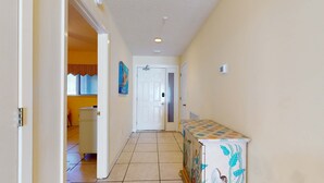 A hallway with a tiled floor, a white door at the end, and a cabinet with a colorful design. - Waterfront Condo with Balcony, Washer/Dryer & Shared Pool (Navarre Beach)