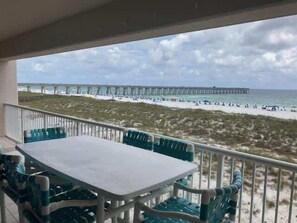 A balcony with a table and chairs, overlooking a beach with a pier in the distance. - Waterfront Condo with Balcony, Washer/Dryer & Shared Pool (Navarre Beach)