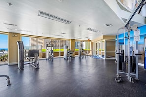 Ein Fitnessstudio mit verschiedenen Trainingsgeräten, großen Fenstern und Blick auf Gebäude.