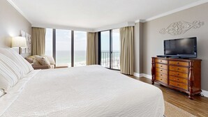 A hotel room with a large bed, a dresser, a television, and a balcony with a view of the ocean. - Gorgeous beachfront condo, shared & and beach access (Panama City Beach)