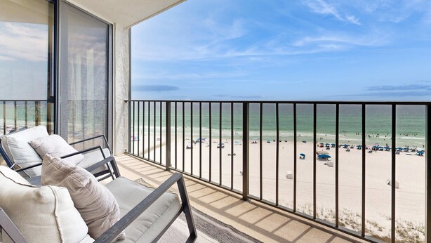 A balcony with a view of a beach, featuring a seating area with cushions and a railing. - Gorgeous beachfront condo, shared & and beach access (Panama City Beach)