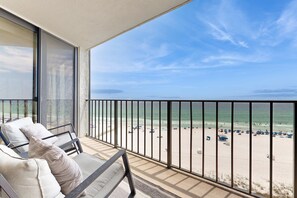 Un balcon donnant sur une plage, avec un espace salon agrémenté de coussins et une balustrade.