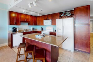 A modern kitchen with wooden cabinets, a granite countertop, a built-in oven, and a refrigerator. - Gulf-view condo steps to beach with balcony, pools, hot tub & gym (Panama City Beach)