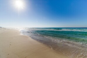 A beach with clear water and a sandy shore under a bright sun. - Gulf-view condo steps to beach with balcony, pools, hot tub & gym (Panama City Beach)