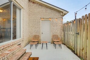 Een bakstenen huis met een witte deur, een houten omheining en buitenplaats met stoelen en een tafel.