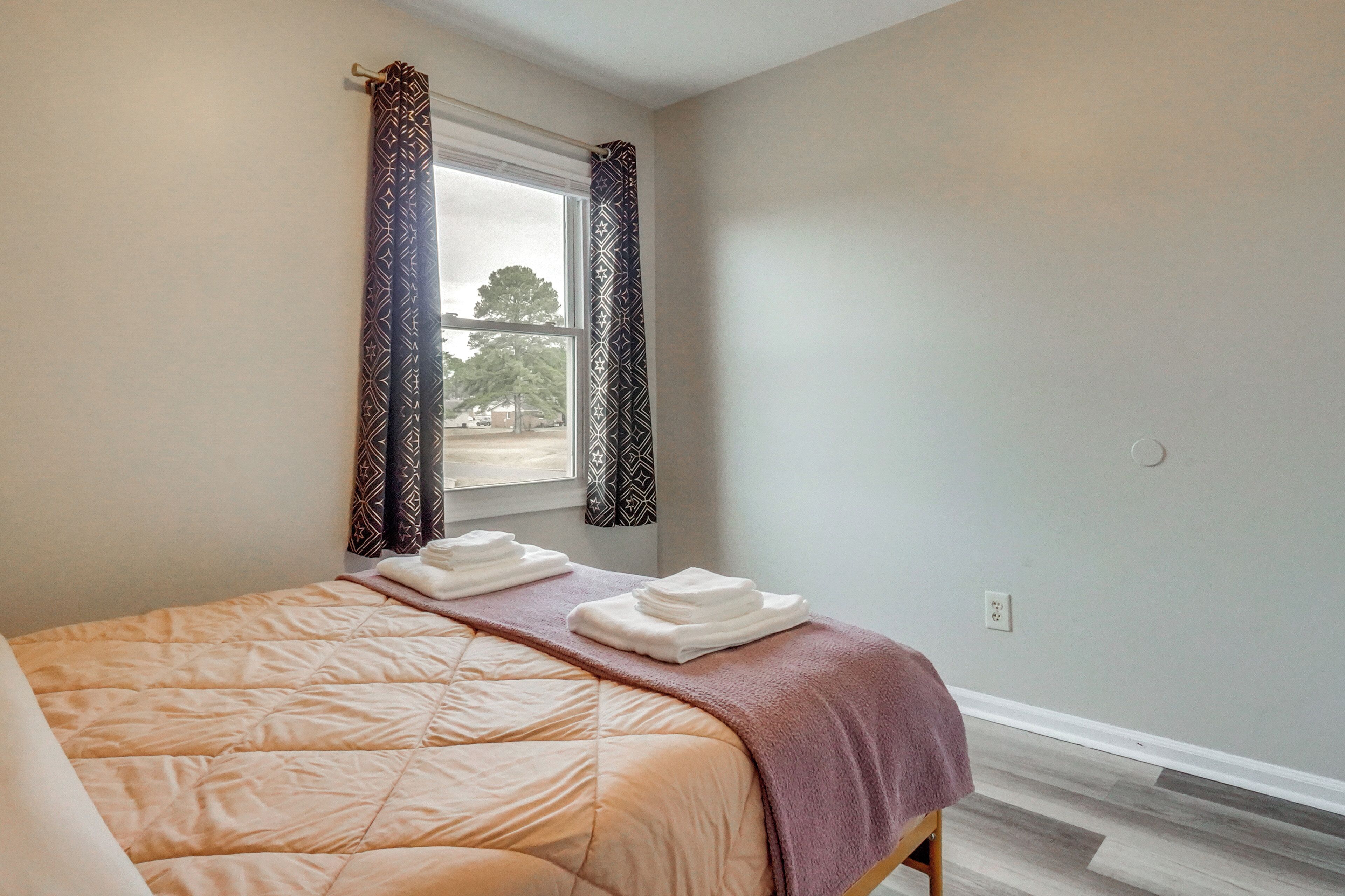 A bedroom with a bed, a window with curtains, and a view of trees and a building outside.