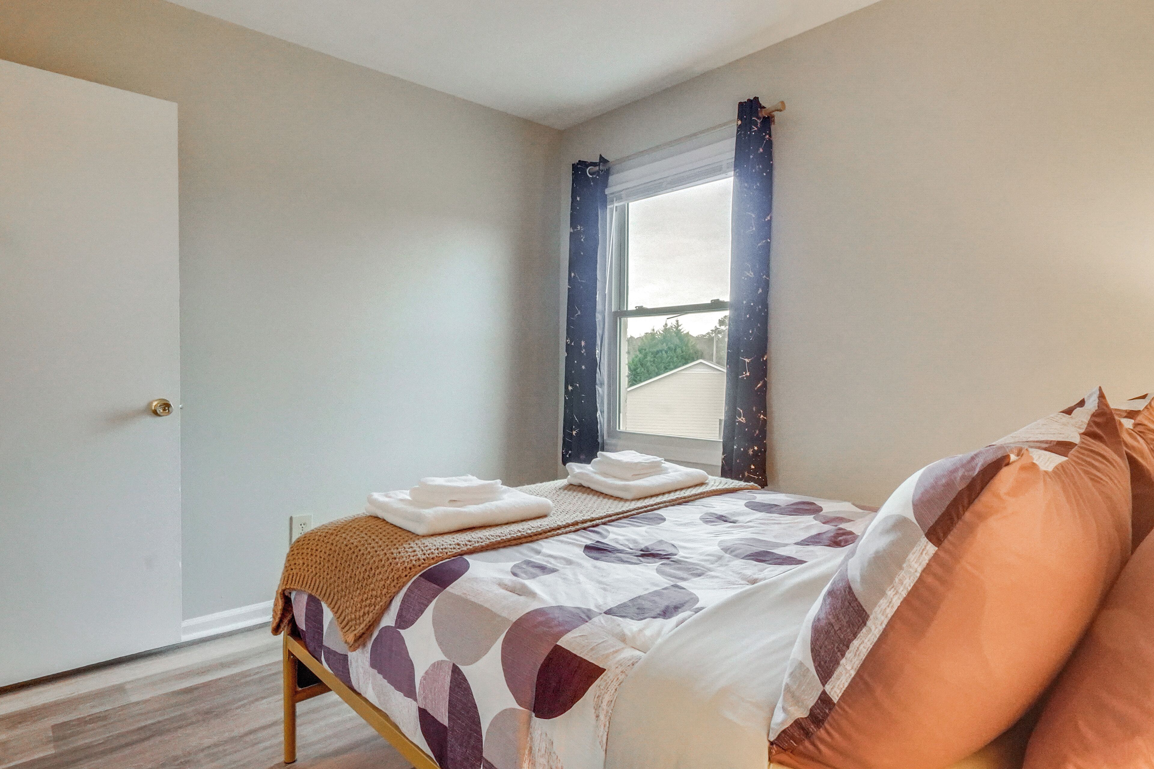 Un dormitorio con cama, ventana con cortinas, una puerta y vista a una casa desde afuera.