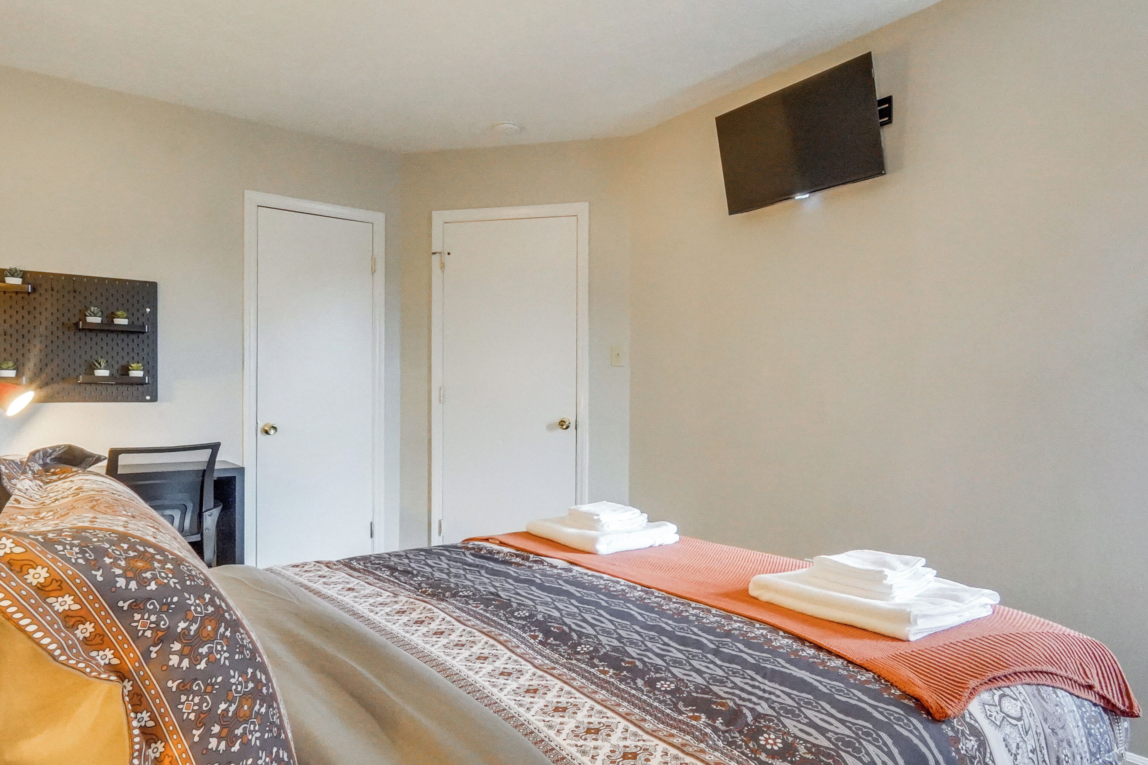 A hotel room with a bed, two doors, a flat-screen TV mounted on the wall, and a wall-mounted pegboard with potted plants.