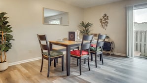 Een eethoek met een houten tafel en stoelen, een grote spiegel aan de wand en een potplant.