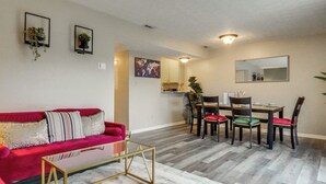 Een woonkamer met een rode bank, een glazen salontafel, en een eetgedeelte met een houten tafel en stoelen.