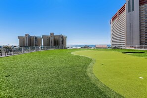 Un terrain de golf bien entretenu, offrant une vue dégagée sur l’océan et deux immeubles de grande hauteur en arrière-plan.