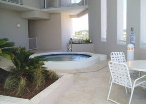 Un espace piscine avec un jacuzzi, des chaises blanches et un petit jardin.