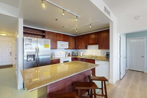 A modern kitchen with granite countertops, stainless steel appliances, and wooden cabinets. - Condo with five pools, hot tubs, saunas, gym, game room, & balcony (Panama City Beach)