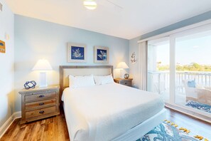 Un dormitorio con una cama grande, dos mesitas de noche con lámparas, un mesón de madera y un balcón con vistas.
