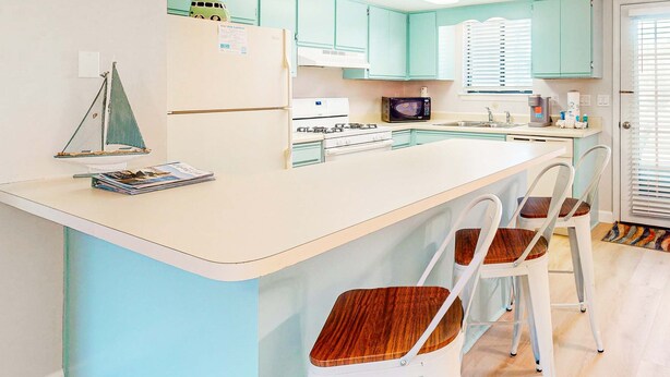 Cucina con mobili color petrolio, un frigorifero bianco, un fornello e un forno a microonde. Sono presenti due sgabelli da bar bianchi con sedute in legno.
