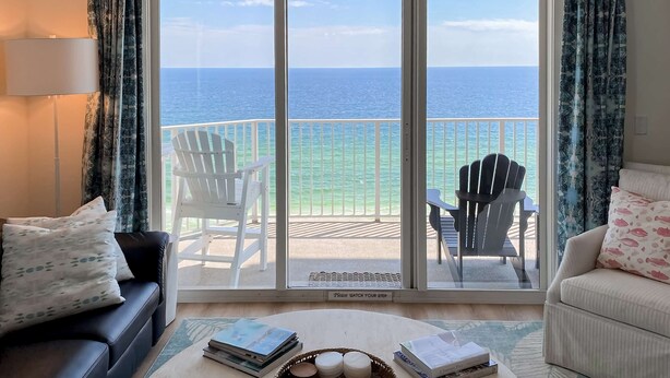 Ein Wohnzimmer mit Meerblick, ein Balkon mit Stühlen und ein Sofa mit Kissen.