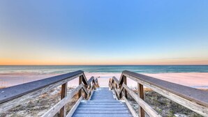 Ein hölzerner Steg führt zu einem Strand unter blauem Himmel.