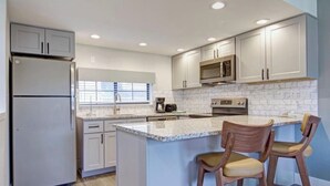 A modern kitchen with a central island, stainless steel appliances, and light-colored cabinetry.
