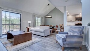 A spacious living area with a large window, a sofa, a striped armchair, a coffee table, and a dining table with chairs.